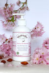 A bottle of Cherry Almond Goat Milk Lotion surrounded by cherry blossoms