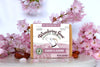 A Bar of cherry almond goat milk soap surrounded by cherry blossoms and almonds