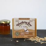 A bar of honey and oats goat milk soap with a jar of honey in the far left and oats in the lower right.