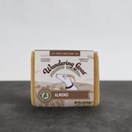 A bar of almond goat milk soap by wandering goat sits on a piece of slate with a white background,