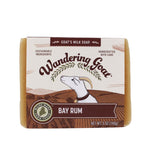 A wrapped bar of Wandering Goat Bay Rum goat milk soap. The wrapper has logo, a goat head and a banner with "Bay Rum" in the text.